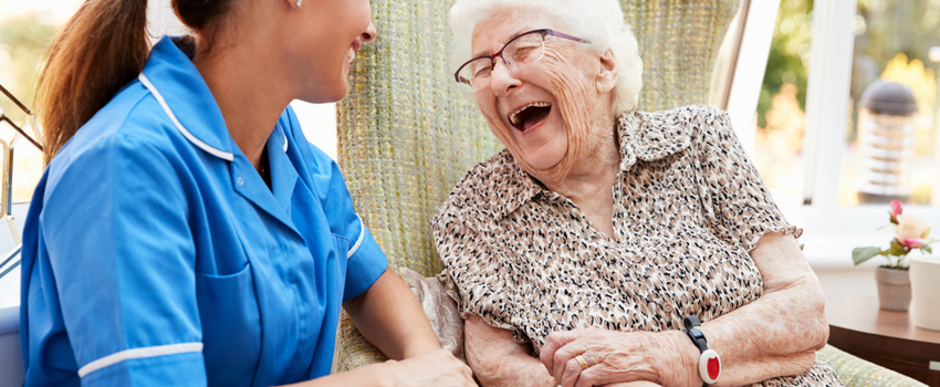 An older woman laughing and talking with a nurse.