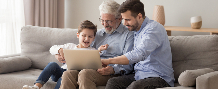 A grandfather using a laptop with his adult son and grandchild.