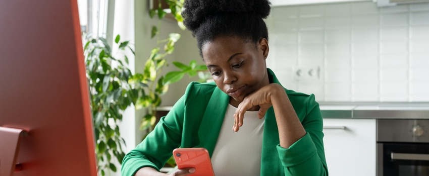 A woman procrastinating on her phone while sitting in front of a computer.