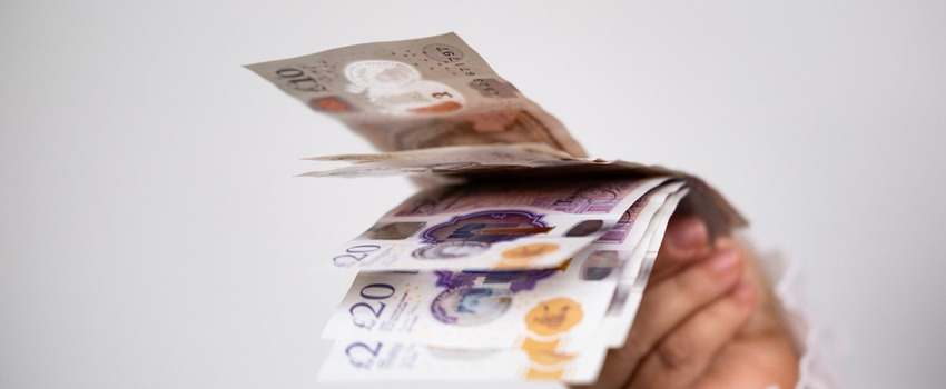 A hand holding UK bank notes.