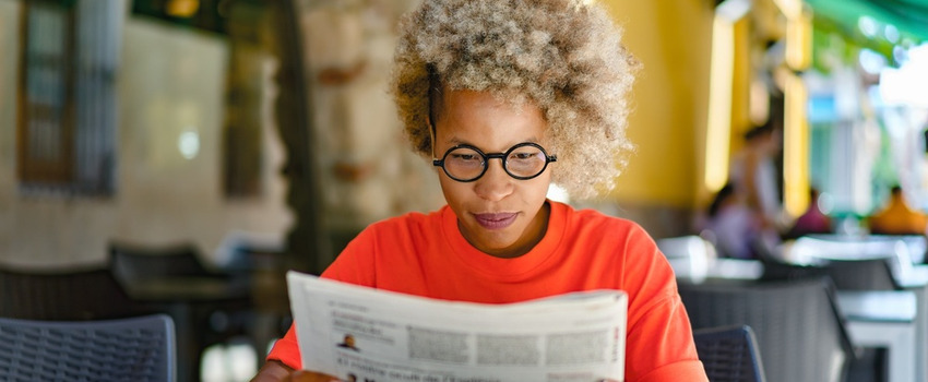 A woman reading a newspaper in a café.